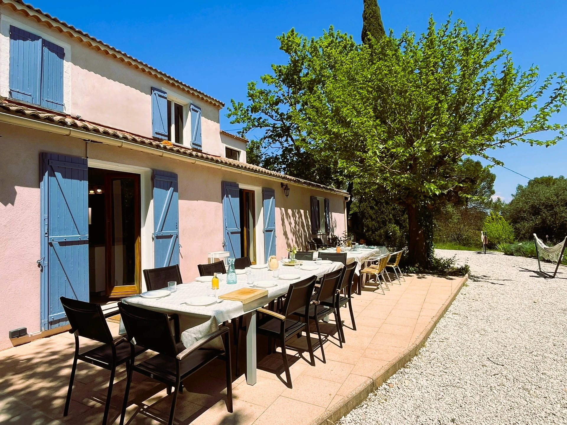 La grande terrasse et sa table, devant les baies vitrées de la maison